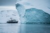 Ein Schiff fährt vor einem Eisberg in der Arktis
