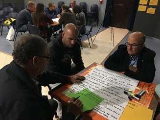 Personen sitzen an Tisch mit Schreibutensilien