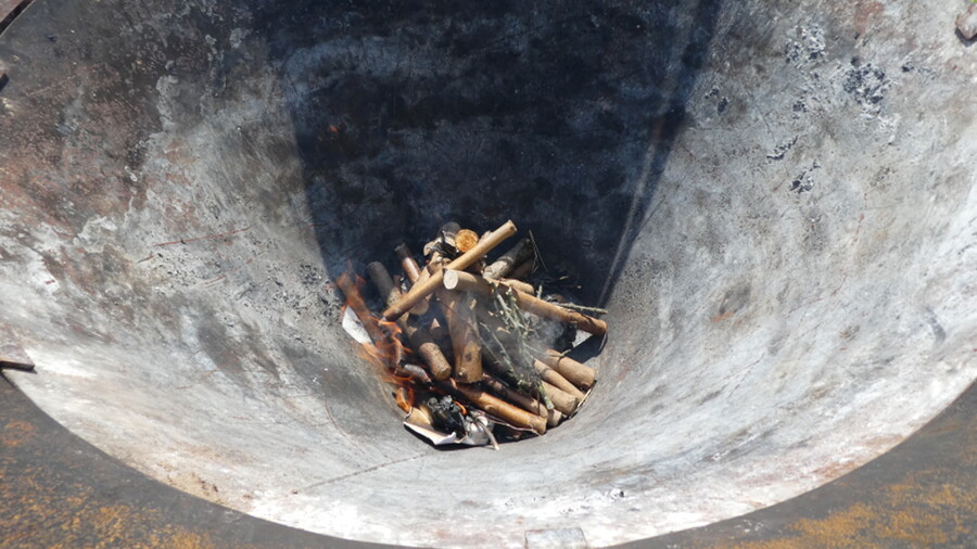 Kleine Äste liegen am Grunde eines trichterförmigen Kilns zur Herstellung von Pflanzenkohle